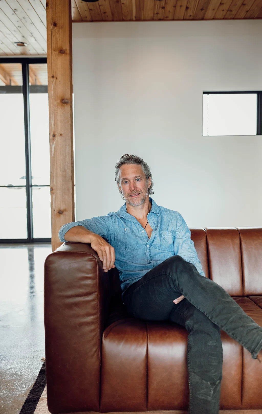Andrew Welker seated on a leather sofa in a timber-framed interior